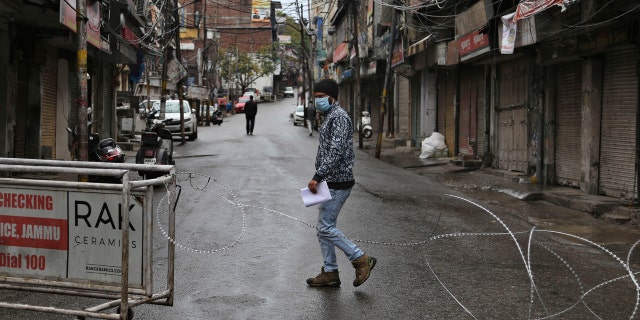 An Indian man wearing a mask walks past a barbed wire erected by authorities as part of enforcing a lockdown as a precautionary measure against COVID-19 in Jammu, India, Tuesday, March 24, 2020.