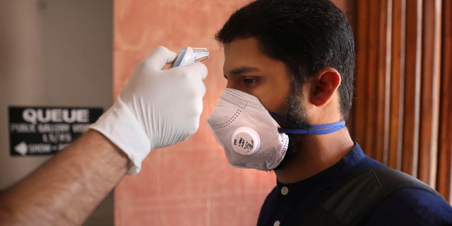 A security official checks the temperature of a visitor as a precaution against the new coronavirus at the Parliament House in New Delhi, India, Tuesday, March 17, 2020.