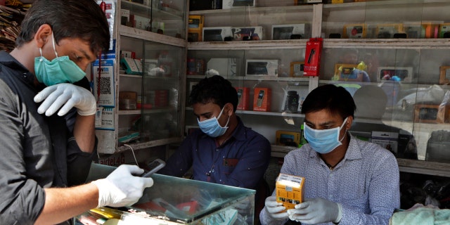 Indian mobile vendors wear protective masks and gloves as a precaution against a new virus at their outlet in Mumbai, India, Tuesday, March 17, 2020.