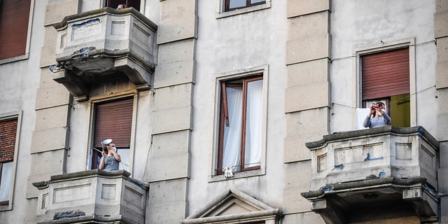 People leaning out of their home's balconies in Milan to play and sing during a flash mob launched throughout Italy to bring people together and try to cope with the emergency of coronavirus. (Claudio Furlan/LaPresse via AP)