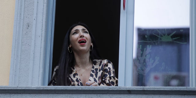 Opera singer Laura Baldassari leans out of her window to sing during a flash mob launched throughout Italy to bring people together and try to cope with the emergency of coronavirus, in Milan, Italy, Friday, March 13, 2020. Italians have been experiencing yet further virus-containment restrictions after Premier Giuseppe Conte ordered restaurants, cafes and retail shops closed after imposing a nationwide lockdown on personal movement. For most people, the new coronavirus causes only mild or moderate symptoms. For some it can cause more severe illness. (AP Photo/Luca Bruno)