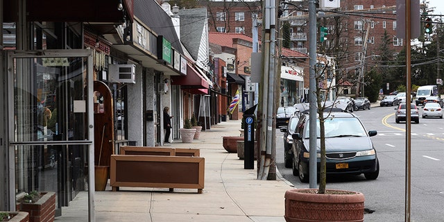 A solitary woman checks her cellphone on a normally busy North Avenue inside what's called a "containment area" in New Rochelle, N.Y., Wednesday, March 11, 2020. State officials on Tuesday called for closing schools, houses of worship and any other spaces were large numbers of people gather within a 1-mile radius (1.6 kilometers) of a point near a synagogue where an infected person had attended events. (AP Photo/Chris Erhmann)