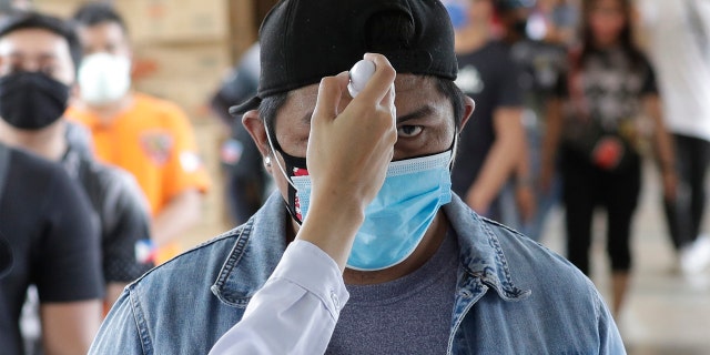 Temperatures are checked before people enter a local city hall during a community quarantine aimed to prevent the spread of the new coronavirus in Manila, Philippines, Tuesday.
