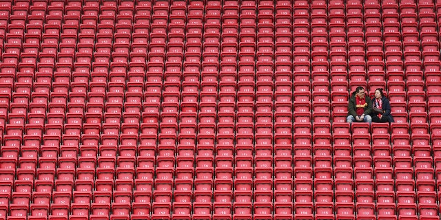 People sit surrounded by empty seats as they wait for the start of the English Premier League soccer match between Liverpool and Bournemouth at Anfield stadium in Liverpool, England, Saturday, March 7, 2020. (AP Photo/Jon Super)