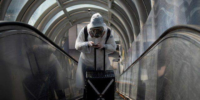 A traveler wearing protective clothing and a full-face mask goes up an escalator after leaving Beijing Railway Station as the country is hit by an outbreak of the novel coronavirus disease (COVID-19), China, March 20, 2020. REUTERS/Thomas Peter 
