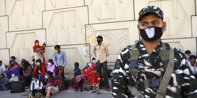 A soldier on guard stands next to migrant workers as they wait for buses along a highway with their families to return to their villages. (REUTERS/Anushree Fadnavis)