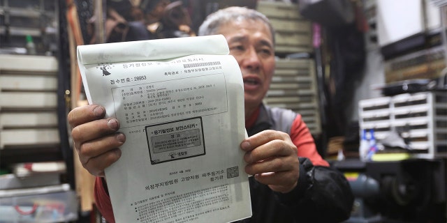 South Korean shoe repairman Kim Byung-rok holds his land ownership registration documents during an interview at his shop in Seoul, South Korea. (AP Photo/Ahn Young-joon)