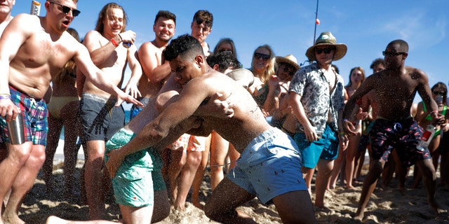 Two men wrestle each other as spring break revelers look on during a contest on the beach, Tuesday, March 17, 2020, in Pompano Beach, Fla.