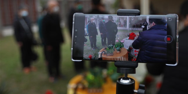 A worker livestreams a funeral ceremony for family members who could not attend the burial at Yuhua cemetery amid the coronavirus outbreak. (China News Service via Getty Images)