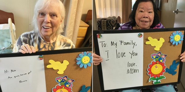 Two residents smile as they hold up signs with messages written to their families,