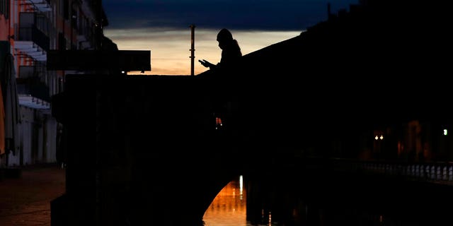 FILE: A woman wearing a face mask checks her phone as she walks at the Naviglio Grande canal in Milan, Italy. (AP)