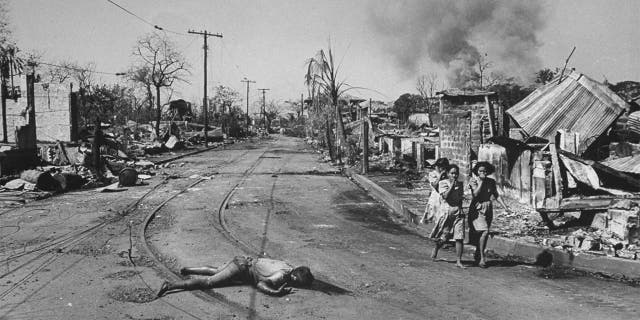 MANILA, PHILIPPINES - FEBRUARY 01: Trio of Filipino women walk past corpse of civilian killed in the battle to retake Manila from occupying Japanese troops.