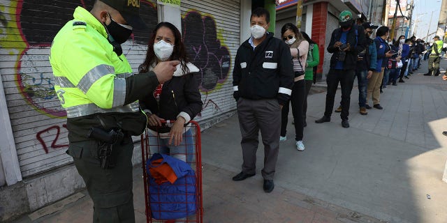 A police officer looks at woman's identification at a public bus station in Soacha on the outskirts of Bogota on Friday. Authorities have called for a complete lockdown of the country to help contain the spread of the new coronavirus, allowing residents to be outside their homes according to their ID numbers. (AP Photo/Fernando Vergara)