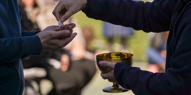 A priest offers a faithful the communion during a Sunday Mass outdoors mass celebrated in their parish soccer field, on the second Sunday of Lent, the first one after Italy's government's prevention measures on public gatherings, in Rome, Sunday, March 8, 2020. (AP Photo/Andrew Medichini)