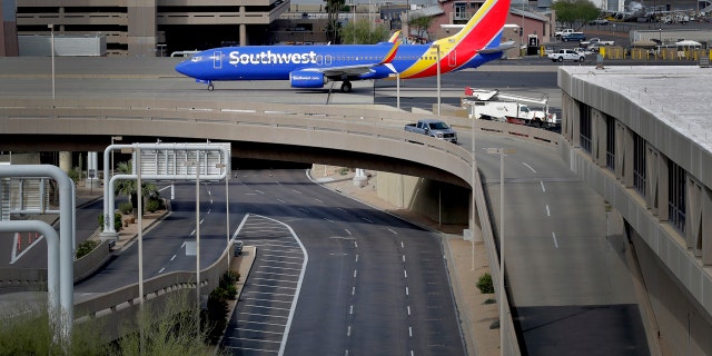 A lone vehicle passes by an arriving jet Wednesday, March 25, 2020, at a typically active Sky Harbor International Airport in Phoenix.