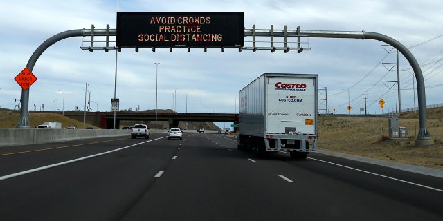 A semi-truck drives down a highway passing an Arizona Department of Transportation public service display Thursday, March 26, 2020, in Chandler, Ariz.