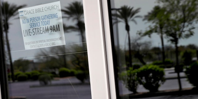 An empty parking lot is reflected in the doors of Grace Bible Church Sunday, March 22, 2020, in Tempe, Ariz. Many houses of worship have suspended all in-person services and programs and moved to online services in compliance with CDC guidelines to promote social distancing in the effort to slow the spread of the COVID-19 coronavirus. (AP Photo/Matt York)