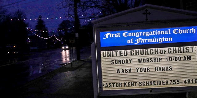 In this March 19, 2020, photo, a church sign reminds townspeople to wash their hands as a car drives under Christmas lights along Main Street in Farmington, N.H. (AP Photo/Charles Krupa)