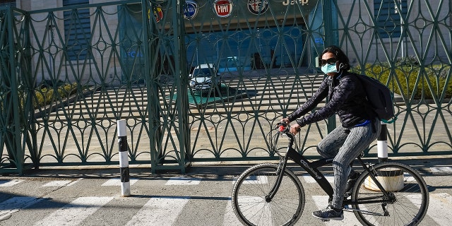 MIRAFIORI FACTORY, TURIN, ITALY - 2020/03/11: A woman wearing a respiratory mask rides past Fiat Mirafiori car plant that today is part of FCA (Fiat Chrysler Automobiles). FCA temporarily closed four plants (Pomigliano, Melfi, Cassino and Atessa) across Italy to prevent spread of COVID-19 coronavirus. (Photo by Nicolò Campo/LightRocket via Getty Images)