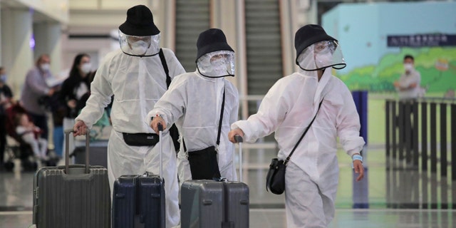 Passengers wear protective suits and face masks as they arrive at the Hong Kong airport, Monday, March 23, 2020.