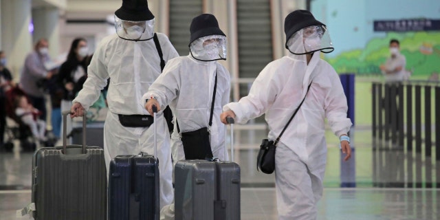 Passengers wear protective suits and face masks as they arrive at the Hong Kong airport, Monday, March 23, 2020.