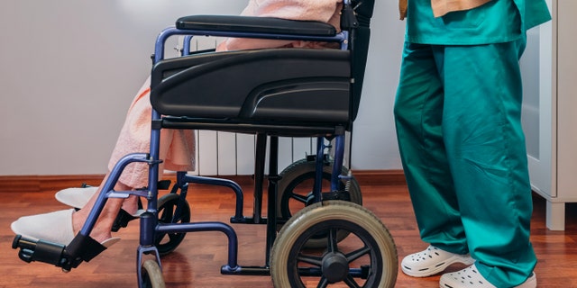 Female doctor carrying elderly female patient in a wheelchair