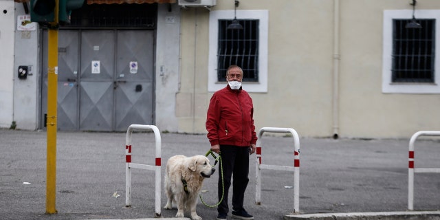 A man strolls with his dog in Rome Friday, March 13, 2020. A sweeping lockdown is in place in Italy to try to slow down the spread of coronavirus epidemic.