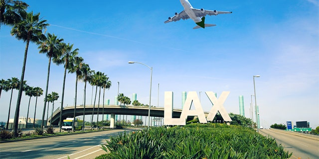 Los Angeles Airport sign full highway with airplane flying overhead.