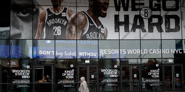 A pedestrian passes an entrance to the Barclays Center in the Brooklyn borough of New York on Thursday, March 12, 2020, after the NCAA's Atlantic 10 Conference Tournament was announced cancelled due to concerns over the COVID-19 coronavirus. (AP Photo/John Minchillo)