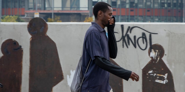 A man uses his hand to cover his nose as he walks along a downtown street Johannesburg, South Africa, Monday, March 16, 2020.