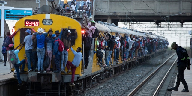 Train commuters hold on to the side of an overcrowded passenger train in Soweto, South Africa, Monday, March 16, 2020.