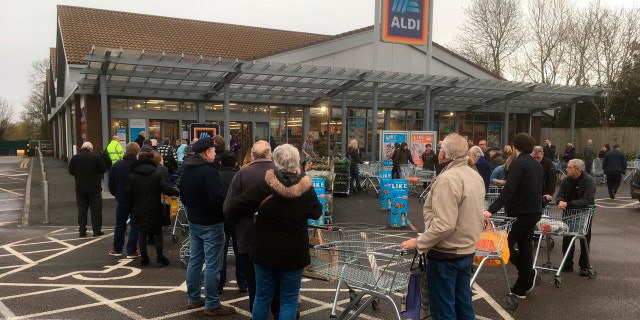 Early shoppers queue and wait in line for the opening of a supermarket in Rugby, England, Thursday, March 19, 2020.