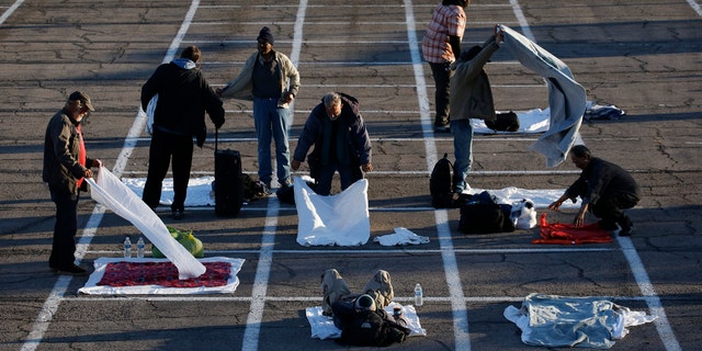 People prepare places to sleep in area marked by painted boxes on the ground of a parking lot at a makeshift camp for the homeless Monday, March 30, 2020, in Las Vegas.