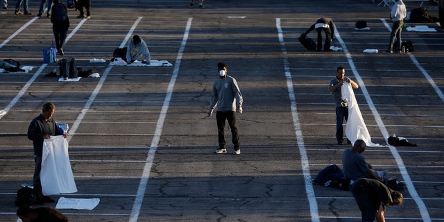 People prepare to sleep in areas marked by painted boxes on the ground of a parking lot at a makeshift camp for the homeless Monday, March 30, 2020, in Las Vegas.