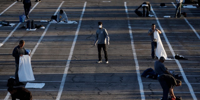 People prepare to sleep in areas marked by painted boxes on the ground of a parking lot at a makeshift camp for the homeless Monday, March 30, 2020, in Las Vegas.