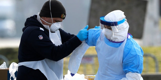 In this March 25, 2020 photo, medical personnel help each other at a federal COVID-19 drive-thru testing site in the parking lot of Walmart in North Lake, Ill. (AP Photo/Nam Y. Huh)