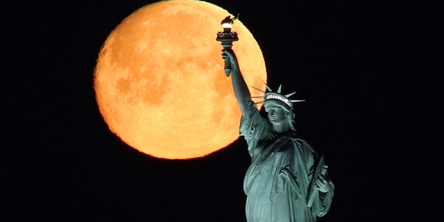 An almost full moon at 97.6 percent sets behind the Statue of Liberty on March 8, 2020 in New York City.