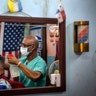 Barber Eugenio Lafargue wearing a protective face mask as a precaution against the spread of the coronavirus is reflected in a mirror as he styles a customer's hair, in Havana, Cuba, March 25, 2020. 