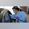 A nurse at a drive-up coronavirus testing station set up by the University of Washington Medical Center uses a swab to take a sample from the nose of a person in a car in Seattle, Wash., March 13, 2020.