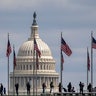 People walk among U.S. flags with the U.S. Capitol in the background, Sunday, March 15, 2020, in Washington. House Speaker Nancy Pelosi, D-Calif., said Congress has started work on a new coronavirus aid package after the one just approved by the House early Saturday.