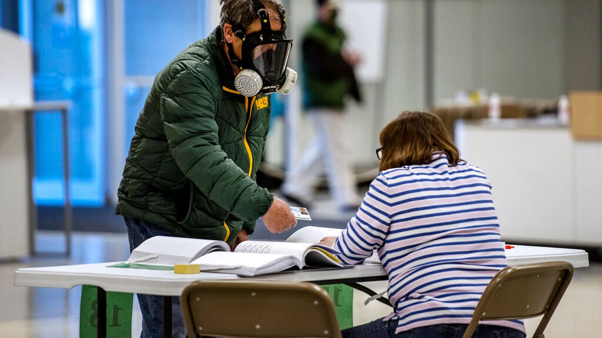 Robert Forrestal, left, wears a full face chemical shield to protect against the spread of coronavirus, as he votes Tuesday, April 7, 2020, at the Janesville Mall in Janesville, Wis. Hundreds of voters in Wisconsin are waiting in line to cast ballots at polling places for the state's presidential primary election, ignoring a stay-at-home order over the coronavirus threat. (Angela Major/The Janesville Gazette via AP)