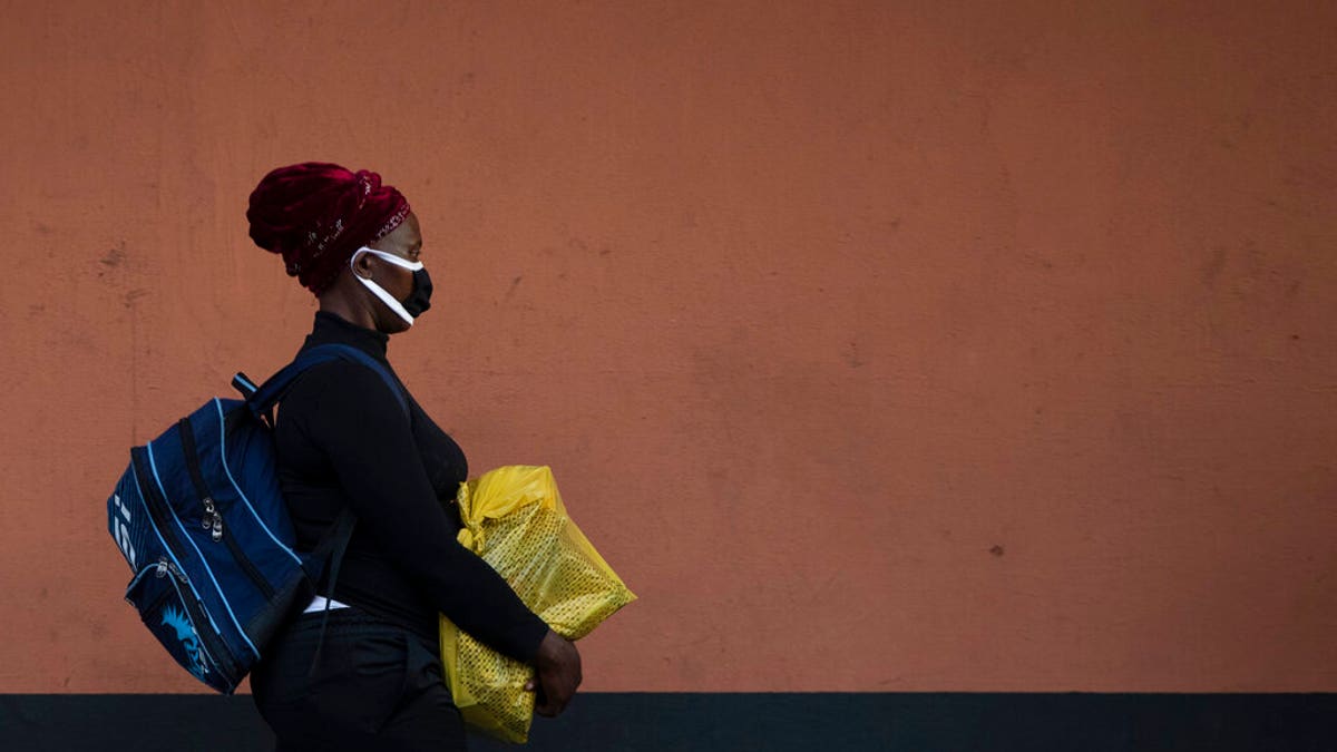 A woman, wearing a protective mask as a precaution against the spread of the new coronavirus, carries her shopping as she walks on the street in Johannesburg, South Africa.
