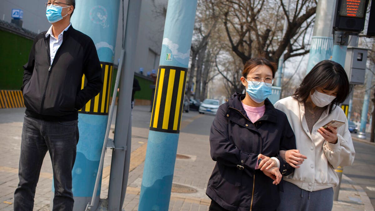 People wearing face masks wait to cross a street in Beijing, on March 31, 2020. China on Tuesday reported just one new death from the coronavirus and a few dozen new cases, all brought from overseas. (AP Photo/Mark Schiefelbein)