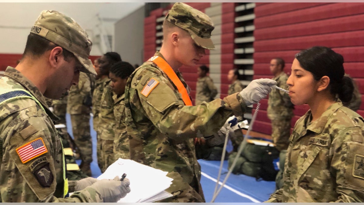 In this image provided by the U.S. Army, recent Army basic combat training graduates have their temperatures taken as they arrive at Fort Lee, Va, on March 31, 2020, after being transported using sterilized buses from Fort Jackson, S.C. (U.S. Army via AP)