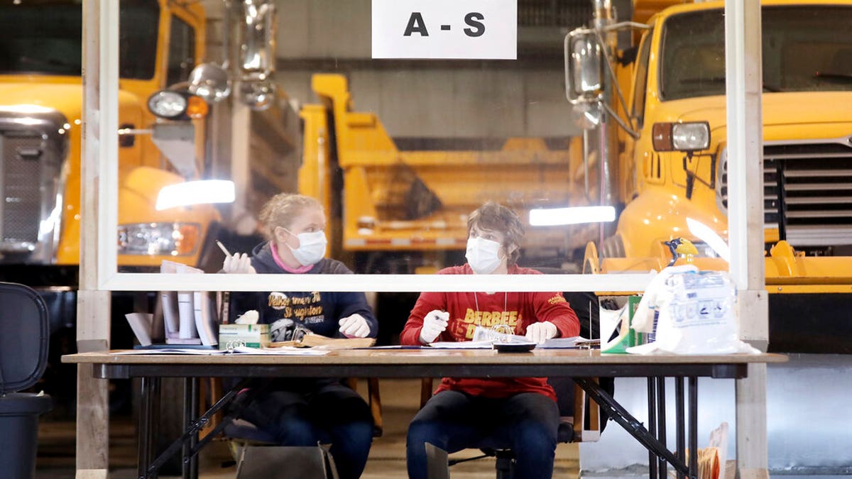 Sisters Kelly and Teal Rowe work behind a plexiglass barrier while waiting to verify voters at the town's highway garage facility, Tuesday, April 7, 2020, in Dunn, Wis. Voters in Wisconsin are casting ballots at polling places for the state's presidential primary election, ignoring a stay-at-home order over the coronavirus threat. (John Hart/Wisconsin State Journal via AP)