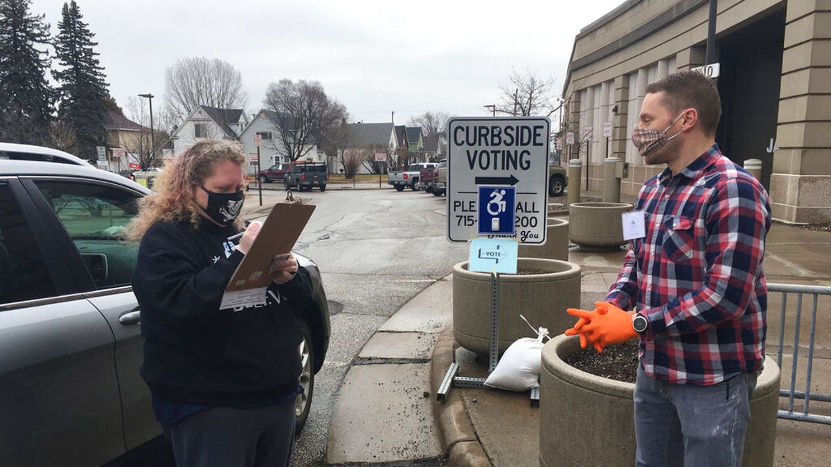 Richard Kaufman, right, a volunteer election official in Superior Wis., helps Betty Bockovich cast a vote at a curbside voting station set up outside the Government Center in Superior, Wis., Tuesday, April 7, 2020. Voters could ring a doorbell and poll workers would come outside to help them vote in the state's presidential primary election if they didn't want to go inside to cast their ballots because of the COVID-19 outbreak. (Dan Kraker/Minnesota Public Radio via AP)