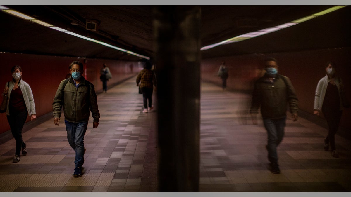 Passengers wearing face masks to prevent the spread of coronavirus, walk along a tunnel connecting platforms in a metro station in Barcelona, Spain, Wednesday, April 15, 2020. Spain has eased this week the conditions of Europe's strictest lockdown, allowing manufacturing, construction and other nonessential activity in an attempt to cushion the economic impact of the pandemic. (AP Photo/Emilio Morenatti)