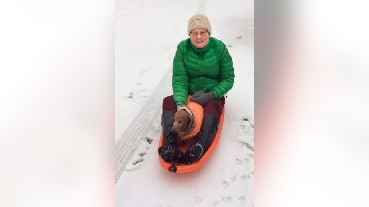 In this December 2016 photo provided by Joyce Smith, Joanne Mellady and her dog Oscar sled down the driveway of her home in Washington, N.H. Mellady, who received a double lung transplant in 2007, died of the coronavirus on March 30, 2020. She was 67.