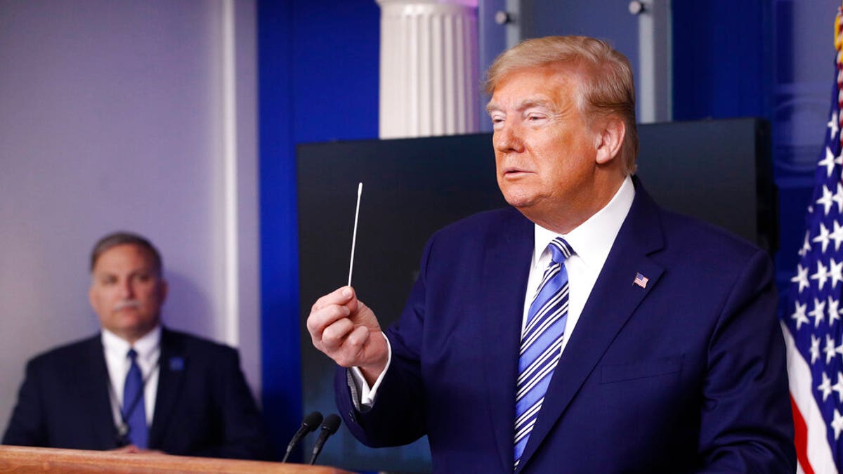 President Donald Trump holds a swab that could be used in coronavirus testing as he speaks during a coronavirus task force briefing at the White House, Sunday, April 19, 2020, in Washington. (AP Photo/Patrick Semansky)