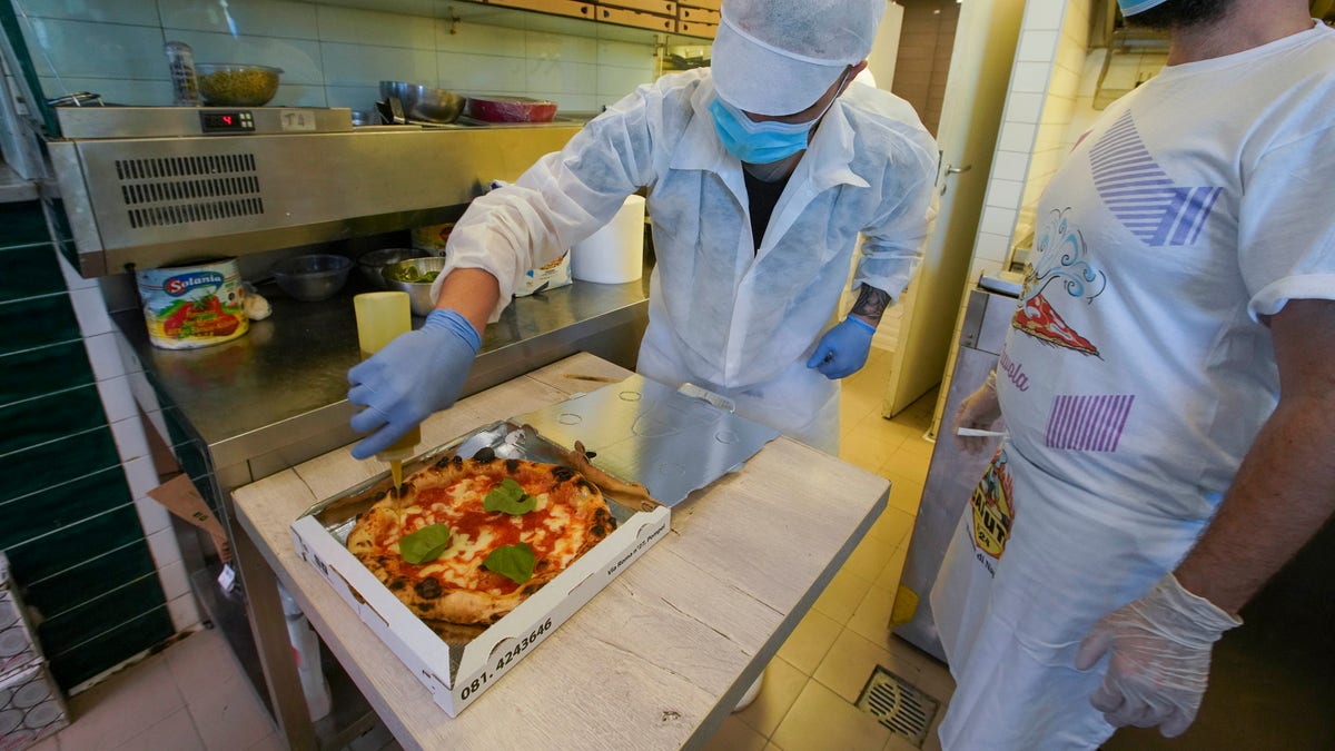 Olive oil is put on a pizza ready to be home delivered, at the Caputo pizzeria in Naples on April 27. The Campania region allowed cafes and pizzerias to reopen for delivery Monday, after a long precautionary closure due to the coronavirus outbreak. (AP Photo/Andrew Medichini)